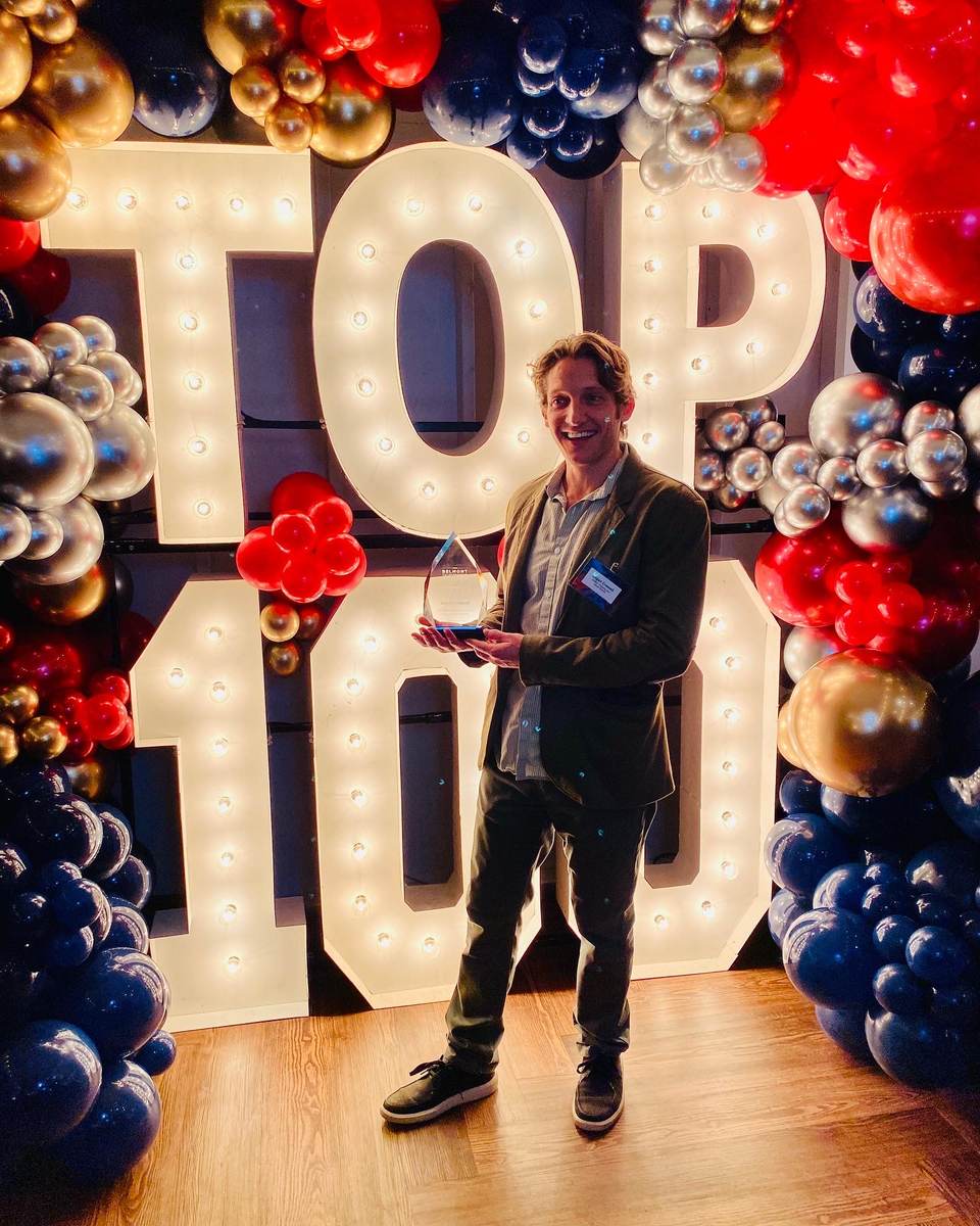 Logan Crowell holding an award in front of the Top 100 display